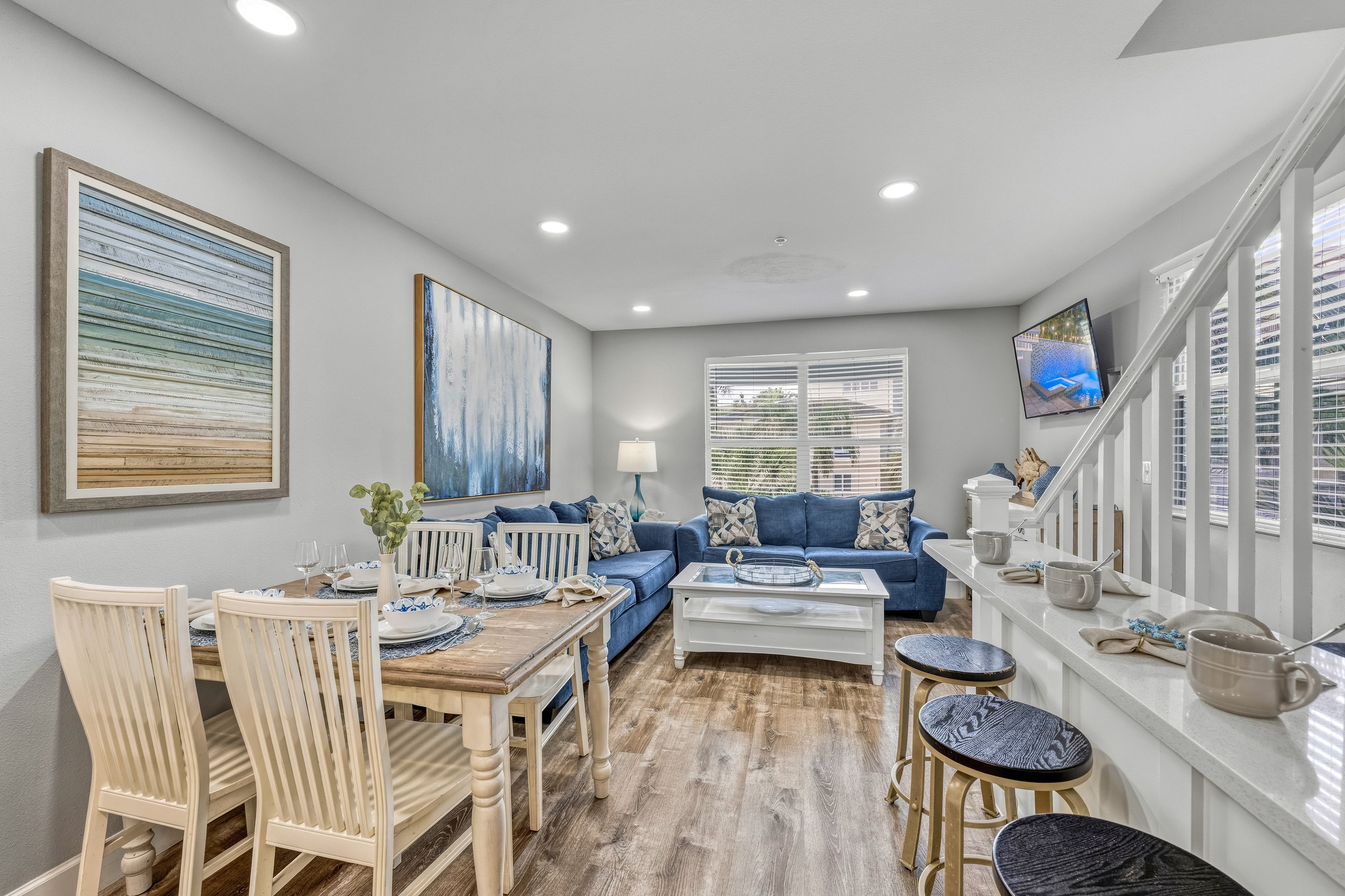 A modern living room with a dining area, a blue sofa set, a coffee table, and a TV mounted on the wall.