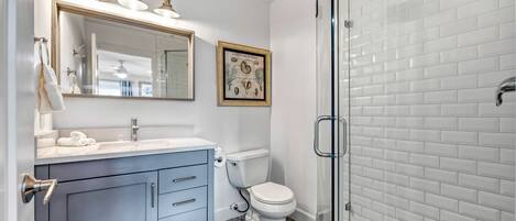 A bathroom with a white toilet, a sink with a mirror, and a shower area.