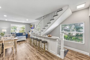 A modern kitchen with a central island, bar stools, and a staircase leading to an upper level.