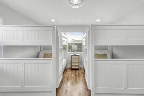 A bunk bed room with a wooden floor, white walls, and a window with blinds.