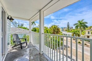 A covered outdoor area with a chair, railing, and a view of a street with buildings and palm trees.