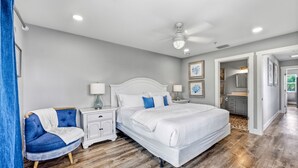 A bedroom with a white bed, a nightstand, a blue chair, and a wooden floor.