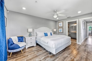 Une chambre avec un lit blanc, une table de chevet, une chaise bleue et un plancher en bois.