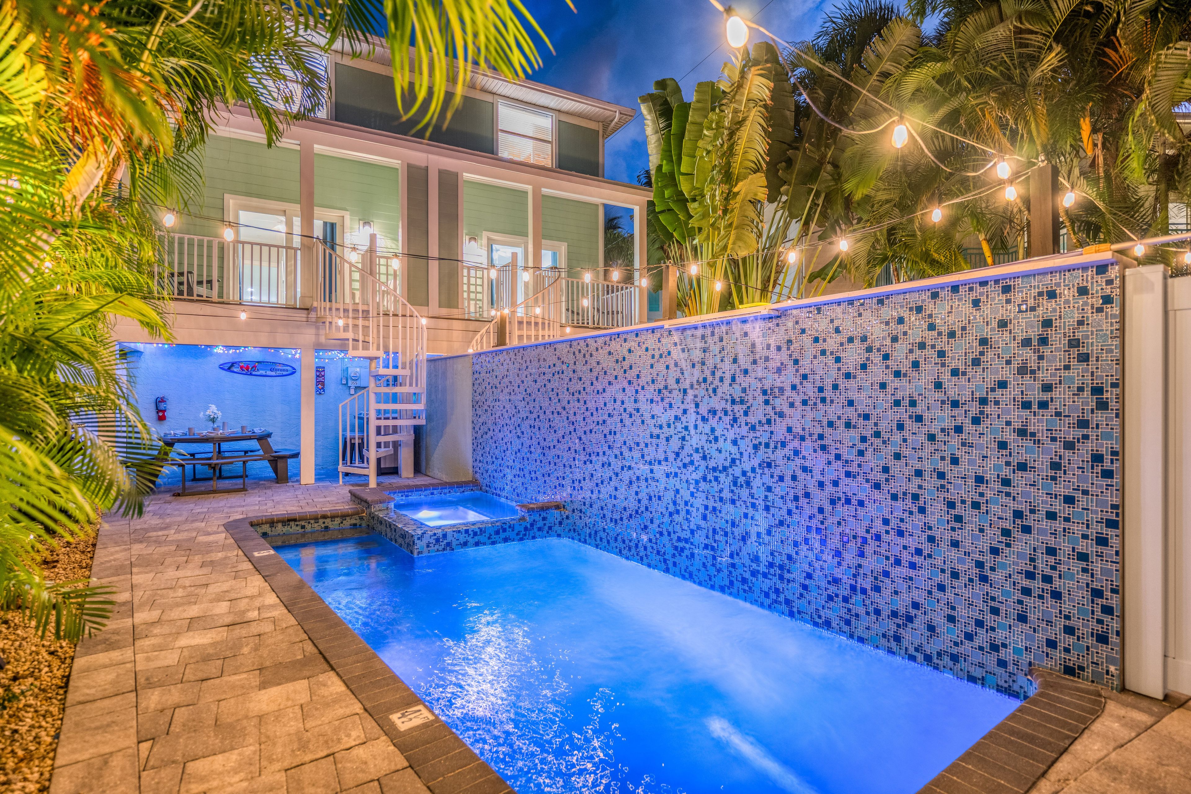 A swimming pool with a tiled wall, a covered seating area, and a staircase leading to an upper level.