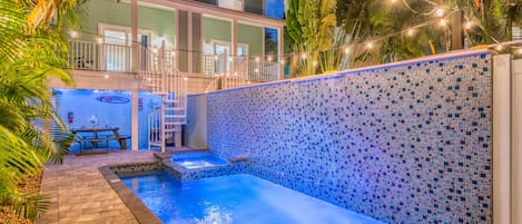 A swimming pool with a tiled wall, a covered seating area, and a staircase leading to an upper level.
