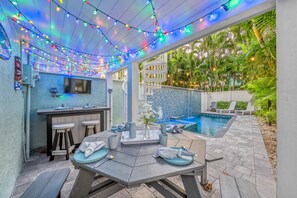 An outdoor patio area with a pool, string lights, and a bar area.