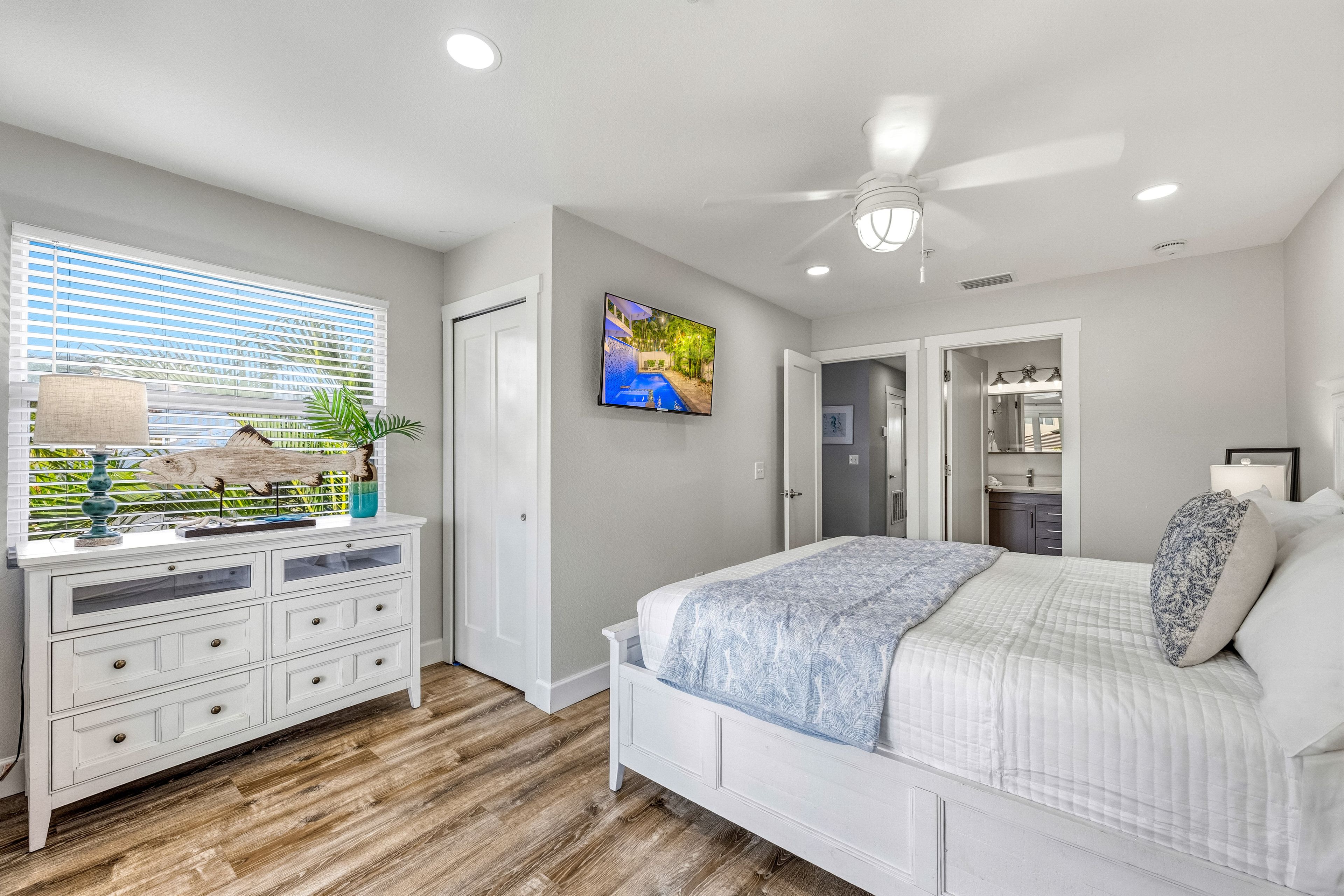 A bedroom with a bed, a dresser, a window with blinds, a ceiling fan, and a painting on the wall.