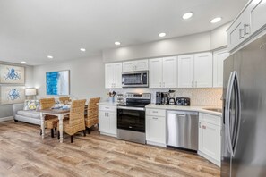 A modern kitchen with white cabinetry, stainless steel appliances, and a dining area with wicker chairs and a wooden table.