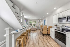 A modern kitchen with a built-in oven, a dining area with wicker chairs, and a staircase with white railings. - NEW! Island Time East | Private Heated Pool, Game Room, In the Heart of Siesta Key Village (Siesta Key)