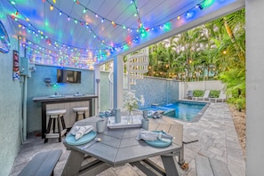 An outdoor patio area with a pool, string lights, and a bar area.
