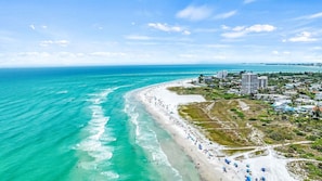 Uma praia costeira com vista clara do oceano, areal arenoso e área residencial com edifícios.