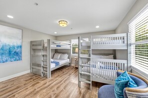A room with bunk beds, a wooden floor, a painting on the wall, and a window with blinds.