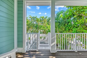 A covered porch with a wooden staircase leading to a pool area, surrounded by lush tropical vegetation.