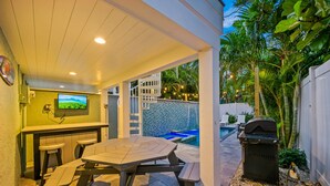 An outdoor patio with a table and chairs, a barbecue grill, and a pool area with a tiled wall. - NEW! Island Time West | Private Heated Pool, Game Room, In the Heart of Siesta Key Village (Siesta Key)