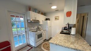 A compact kitchen with white cabinets, a stove, a refrigerator, and a granite countertop. - Vintage Vero Bungalow II (Vero Beach)