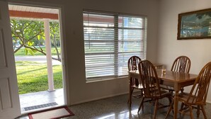 A dining area with a table and chairs, a window with blinds, a door leading outside, and a painting on the wall. - Vintage Vero Bungalow II (Vero Beach)