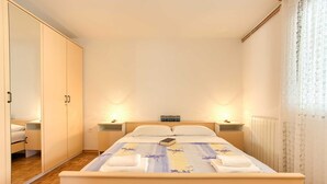 Un dormitorio ordenado con cama, dos mesitas de noche, un armario y una ventana con cortinas.