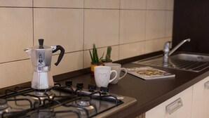 Una cocina con estufa a gas, cafetera, dos tazas, una planta y una revista sobre el mostrador.