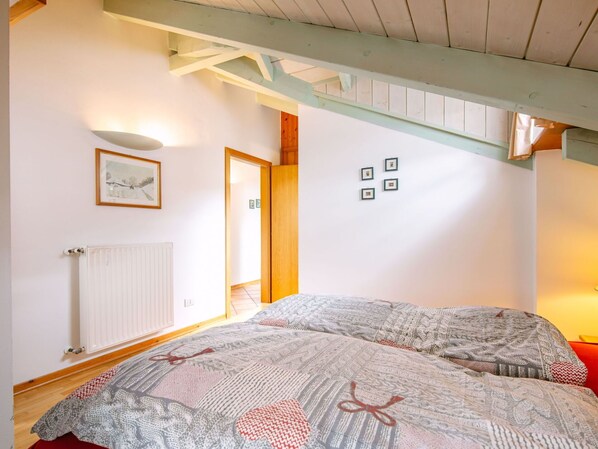 A bedroom with two beds, a radiator, a framed picture, and a wooden ceiling beam.