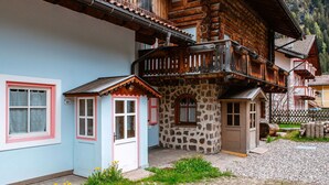 Una casa tradicional de madera con base de piedra, un balcón con barandilla de madera y un patio empedrado.