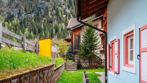 Un estrecho sendero de piedra conduce a una casa de madera con techo empinado, rodeada de abundante vegetación y un paisaje montañoso.