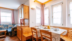 Une cuisine chaleureuse avec des meubles en bois, une table à manger dressée pour deux personnes et un canapé en arrière-plan.
