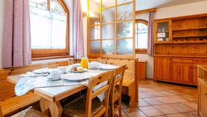 Ein gemütlicher Essbereich mit Holzmöbeln, einem großen Fenster mit satinierten Glasfeldern und einer Küche mit Holzausstattung.