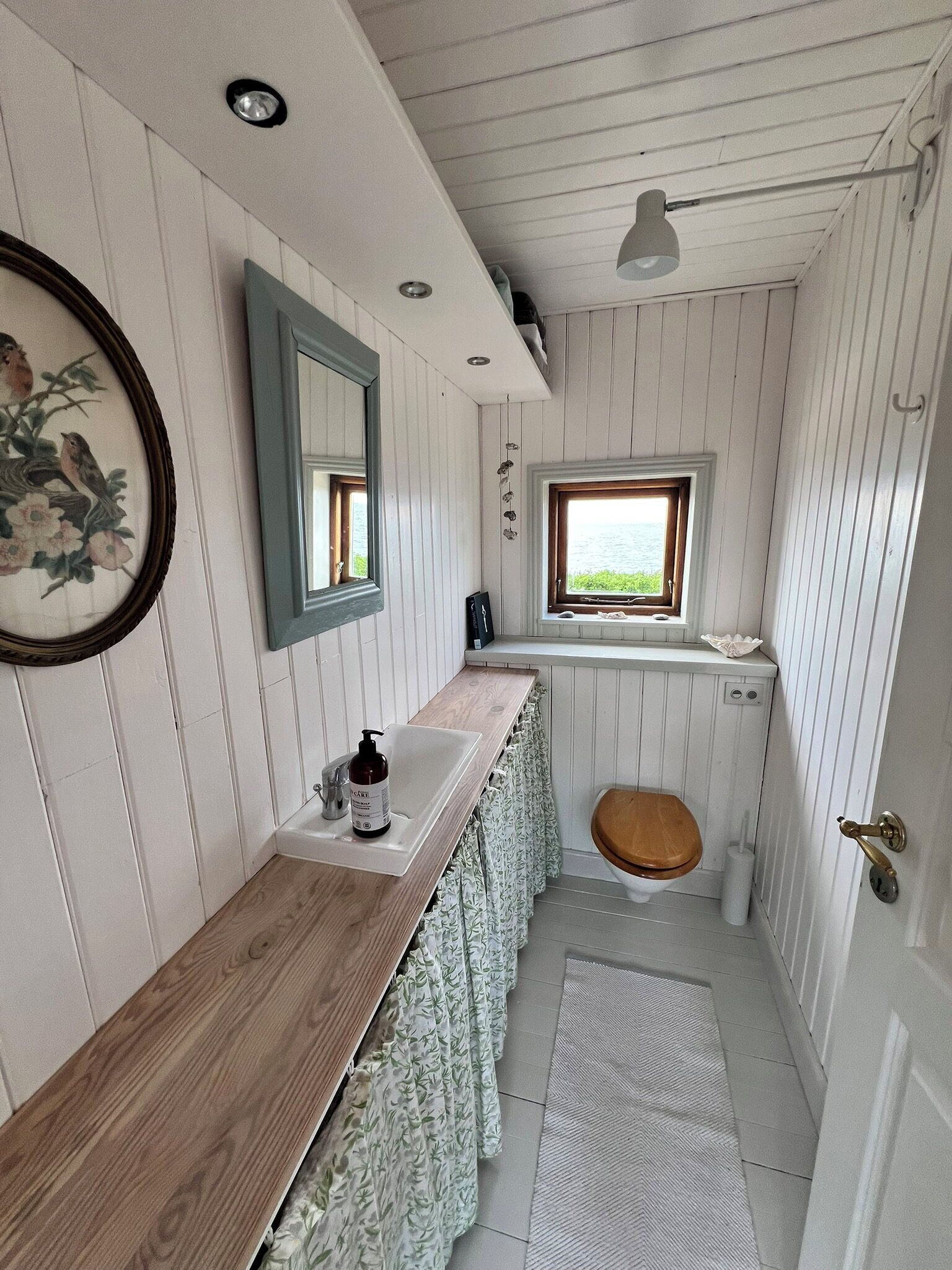 A bathroom with a wooden vanity, a mirror, a window, and a toilet.