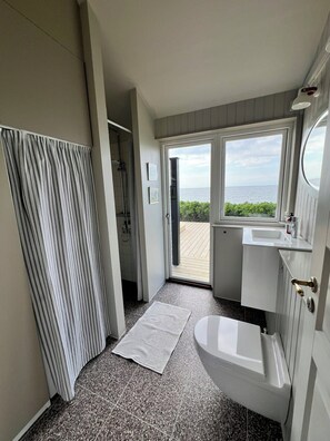 Ein Badezimmer mit Badewanne, Dusche, Waschbecken und einem großen Fenster mit Meerblick.