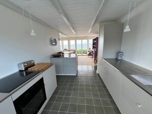 A modern kitchen with a black countertop, white cabinets, and a view of the sea through large windows. - Welcoming holiday home right down to the water (Rørvig)