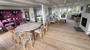 A spacious room with a wooden floor, a round dining table surrounded by wicker chairs, a purple bookshelf, and a fireplace. - Welcoming holiday home right down to the water (Rørvig)