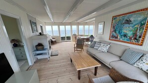 A spacious living area with a wooden floor, a sofa, a table, and a wicker chair. There is a large window with a view of the sea. - Welcoming holiday home right down to the water (Rørvig)