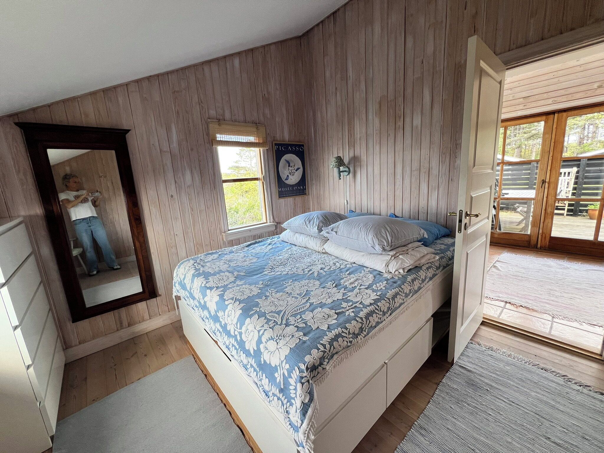 Une chambre à coucher comprenant un lit, un miroir, une fenêtre et une porte donnant sur un espace extérieur.