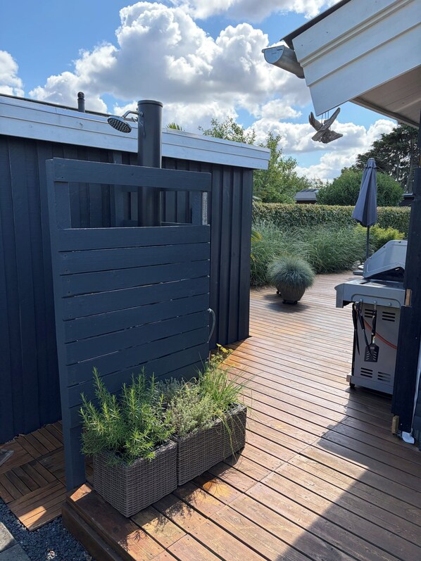 A wooden deck with a dark blue fence, a barbecue grill, and a potted plant.