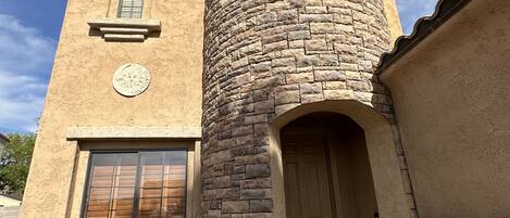 A two-story building with a stone tower, a large window, and a door.