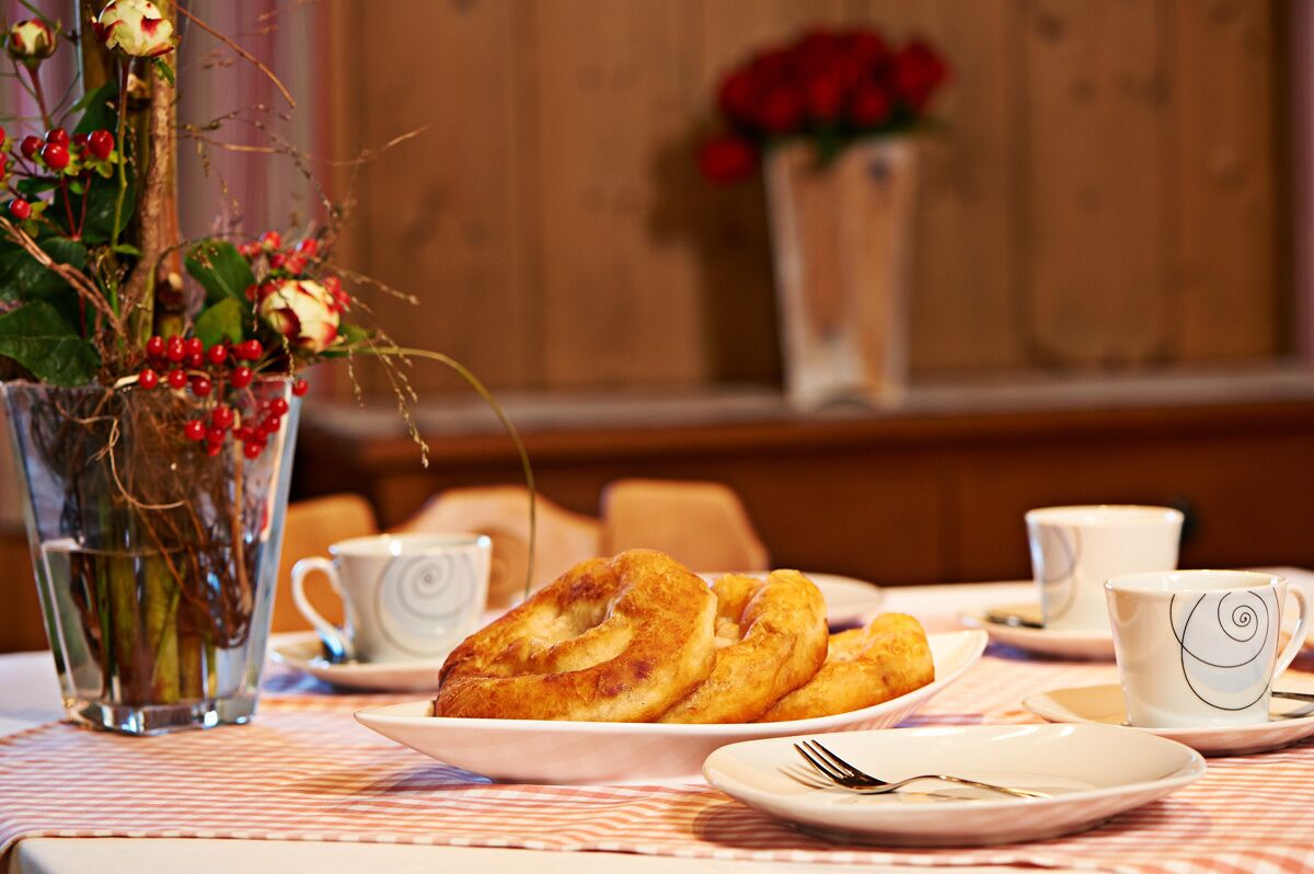A dining table with a plate of pastries, a vase with flowers, and two cups.