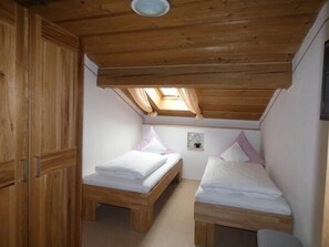 Ein kleines, gemütliches Zimmer mit zwei Holzbett und einem Einbauschrank, sowie einem Dachfenster.