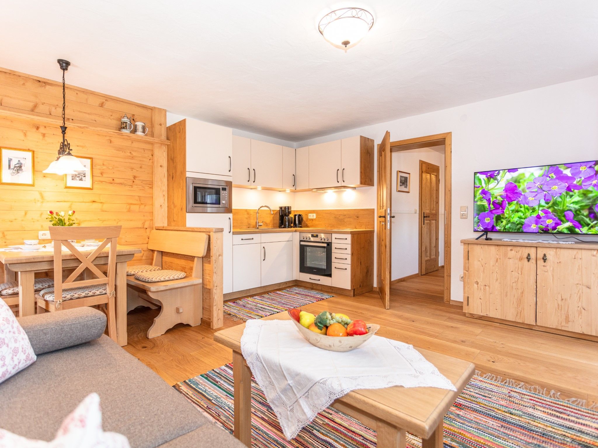 Ein gemütliches Wohnzimmer mit einer Couch, einem Couchtisch mit Früchten und einem Fernseher, der Blumen zeigt.