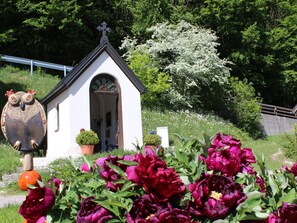 Een kleine witte kerk met een kruis bovenop, omringd door weelderig groen en kleurrijke bloemen.