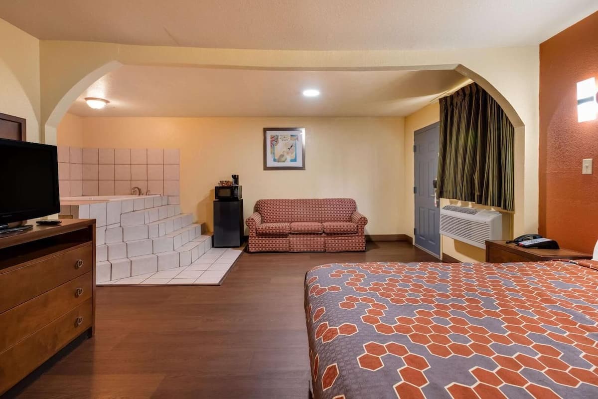 Een slaapkamer met een bed, een televisie, een bank, een magnetron en een trap naar een balkon.