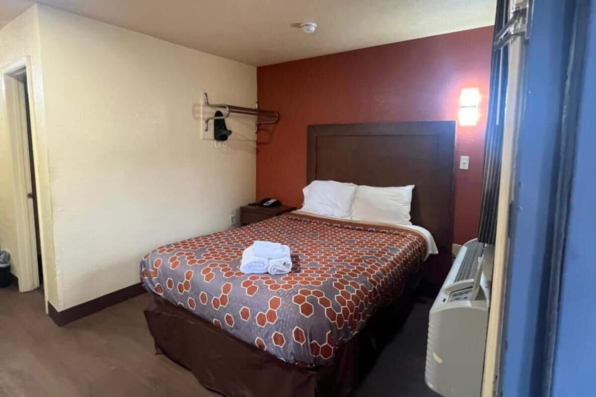 Een hotelkamer met een bed, nachtkastje, telefoon en kachel.