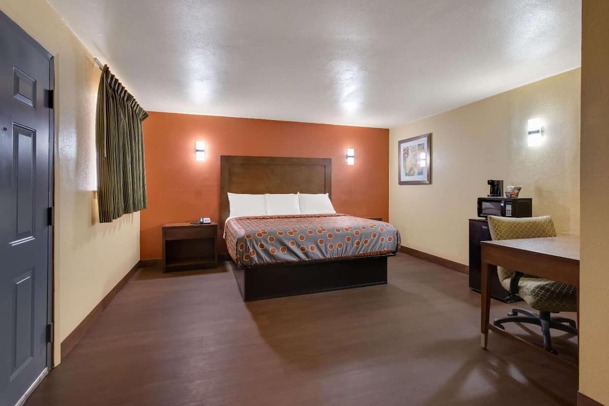 Een hotelkamer met een bed, nachtkastje, lamp en een klein bureau met stoel.