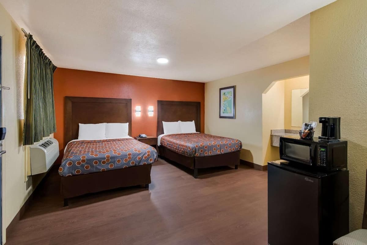Een hotelkamer met twee bedden, een magnetron, een koffiezetapparaat en een klein tafeltje.