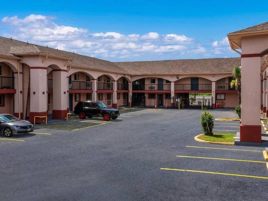 Un hotel con un patio central, varios balcones y un estacionamiento con automóviles.