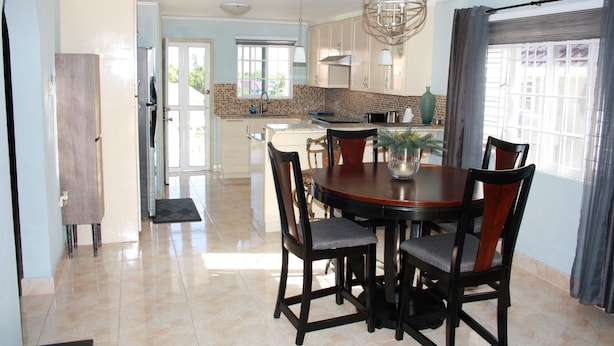 A spacious kitchen with a dining area, featuring a central island, dark wooden chairs, and a hanging light fixture. - Soleil Hartland 122 (St. Ann's Bay)