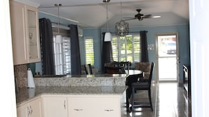A kitchen with white cabinets, a granite countertop, a ceiling fan, and a dining area with a table and chairs. - Soleil Hartland 122 (St. Ann's Bay)
