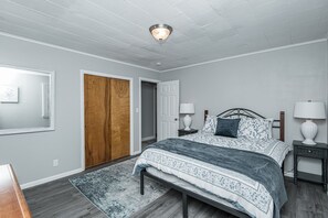 Une chambre à coucher avec un lit, des tables de chevet, une porte en bois et un luminaire au plafond.