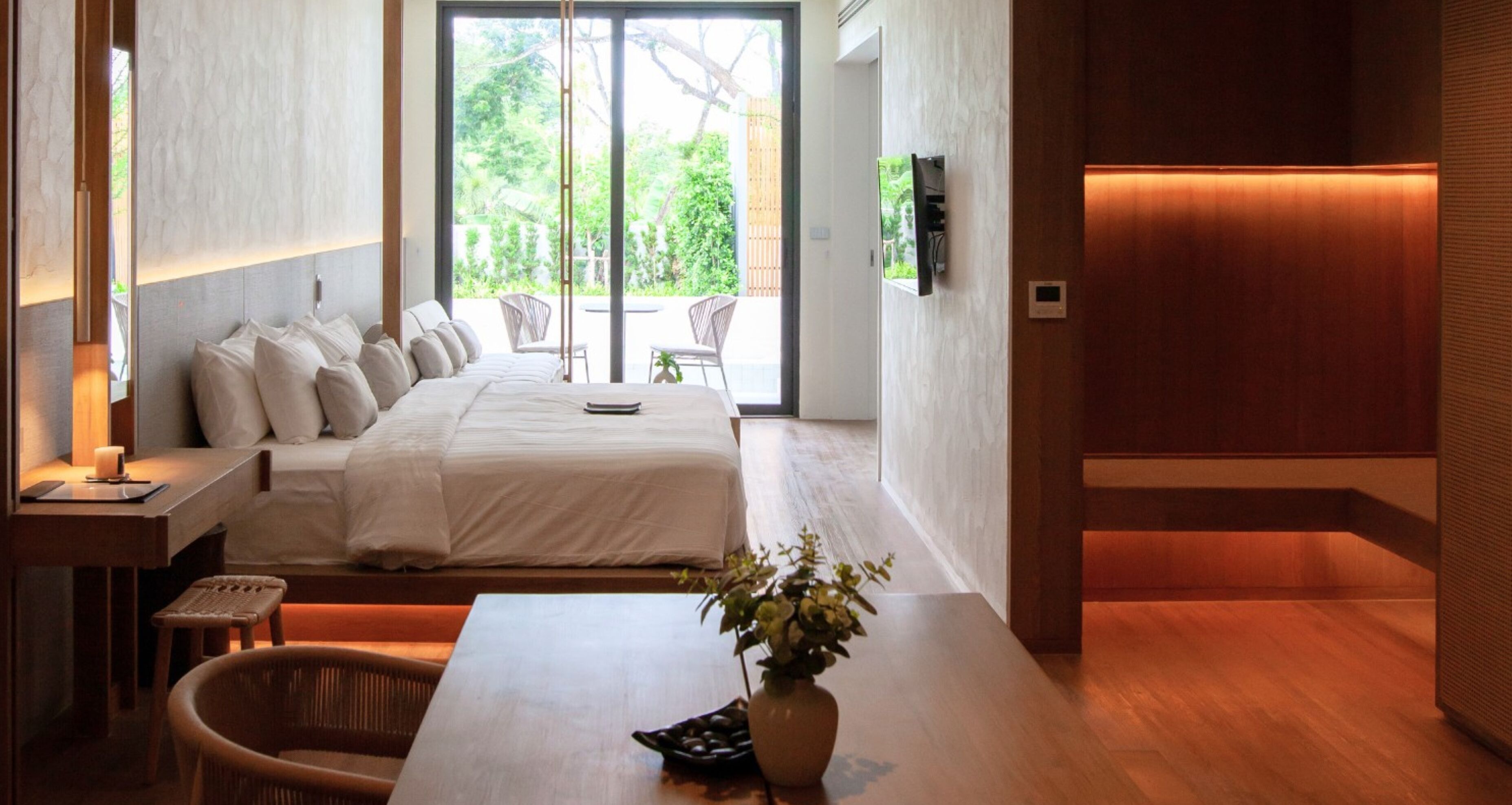 A modern hotel room with a bed, a desk, a chair, and a view of the outdoors.