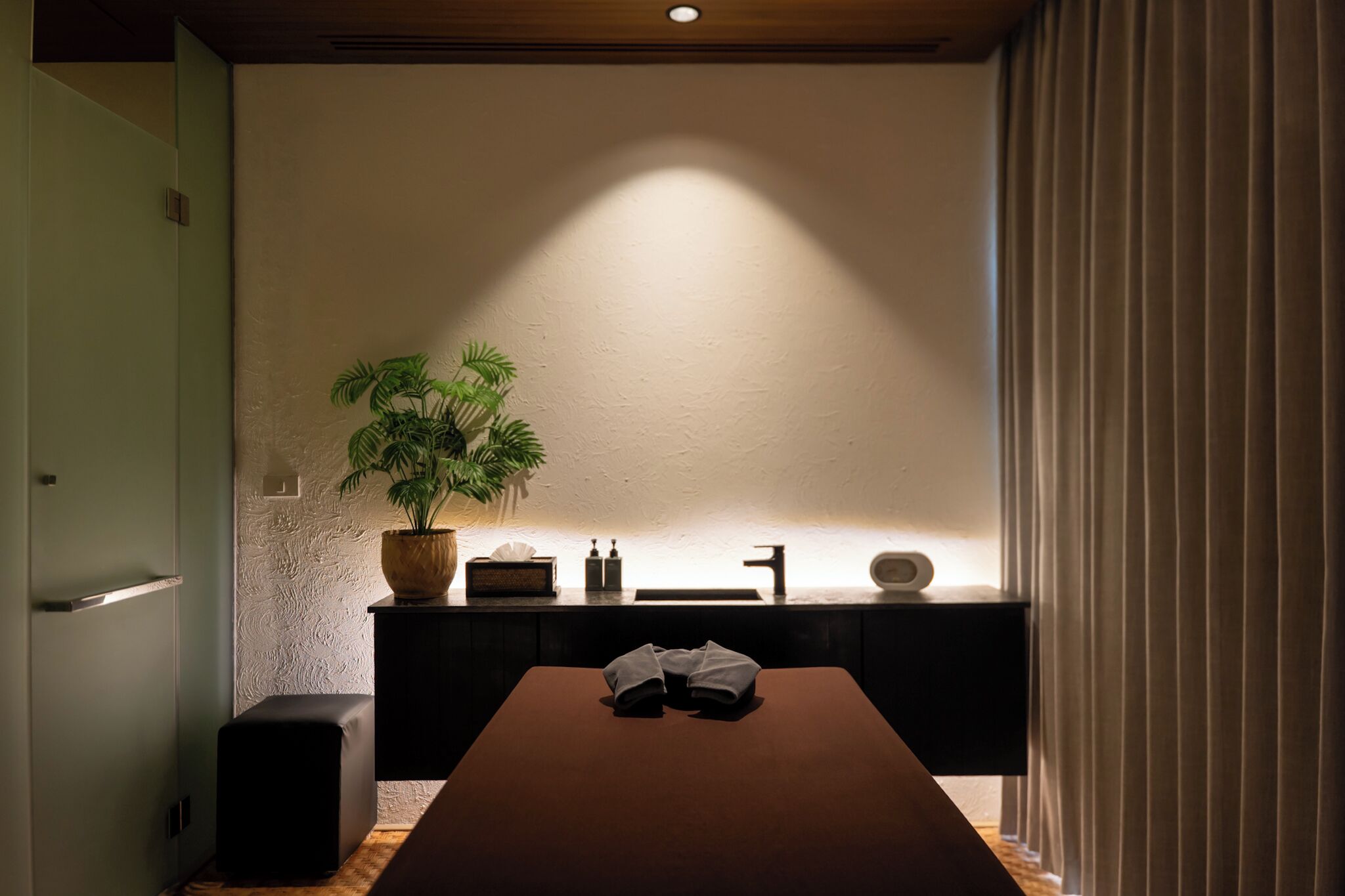 Una habitación minimalista con una mesa de madera, una planta en maceta, un mueble pequeño y una cortina.