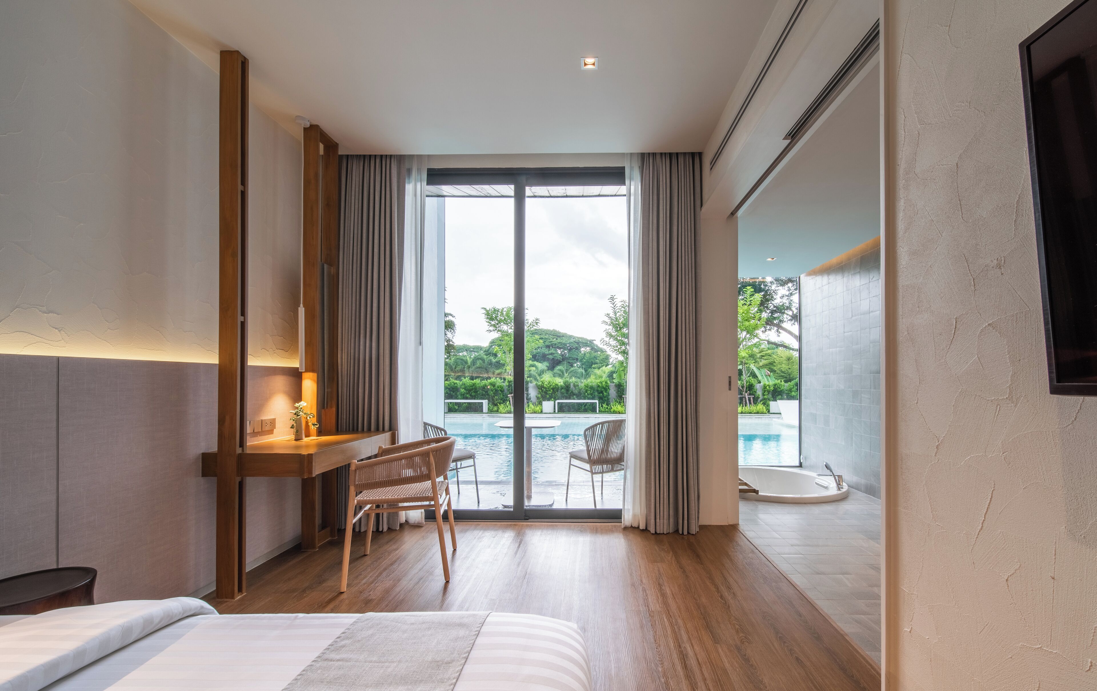 Een moderne hotelkamer met een grote schuifglazen deur naar een zwembad, een houten bureau en een comfortabele zithoek.